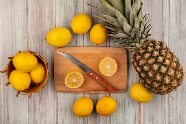 top view of healthy lemons on a bucket with half lemons on a wooden kitchen board with knife with lemons and pineapple isolated on a grey wooden background 141793 84495